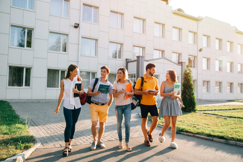 groupe de 5 collegiens qui marche. derriere eux un batiment scolaire